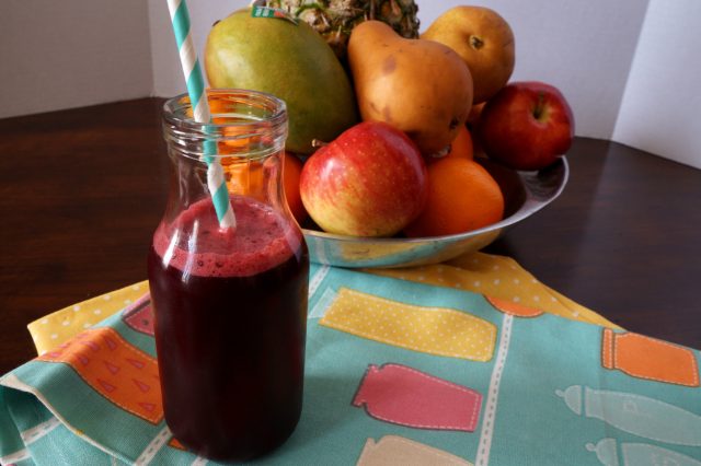 glass bottle of juice with decorative straw and bowl of fruit in the background