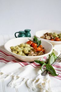 plate of gnocchi with pesto, sausage, and tomatoes