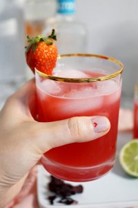 holding a glass of strawberry hibiscus margaritas