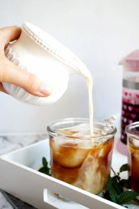 pouring oat milk into the cold brew coffee