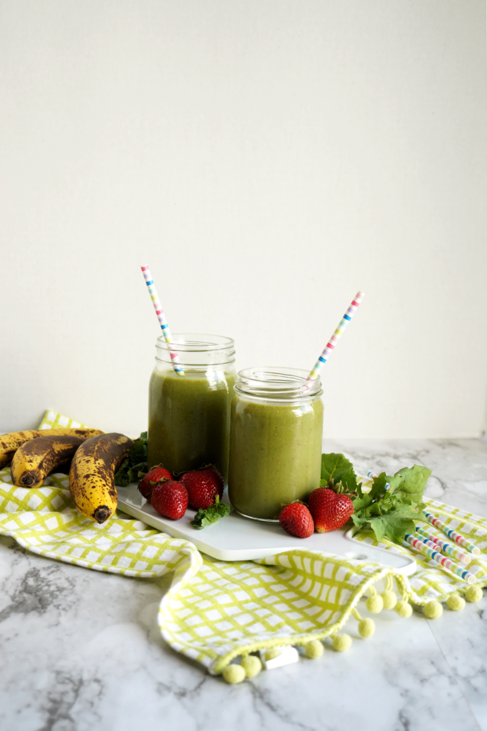 far away shot of two green smoothie mason jars on a white cutting board