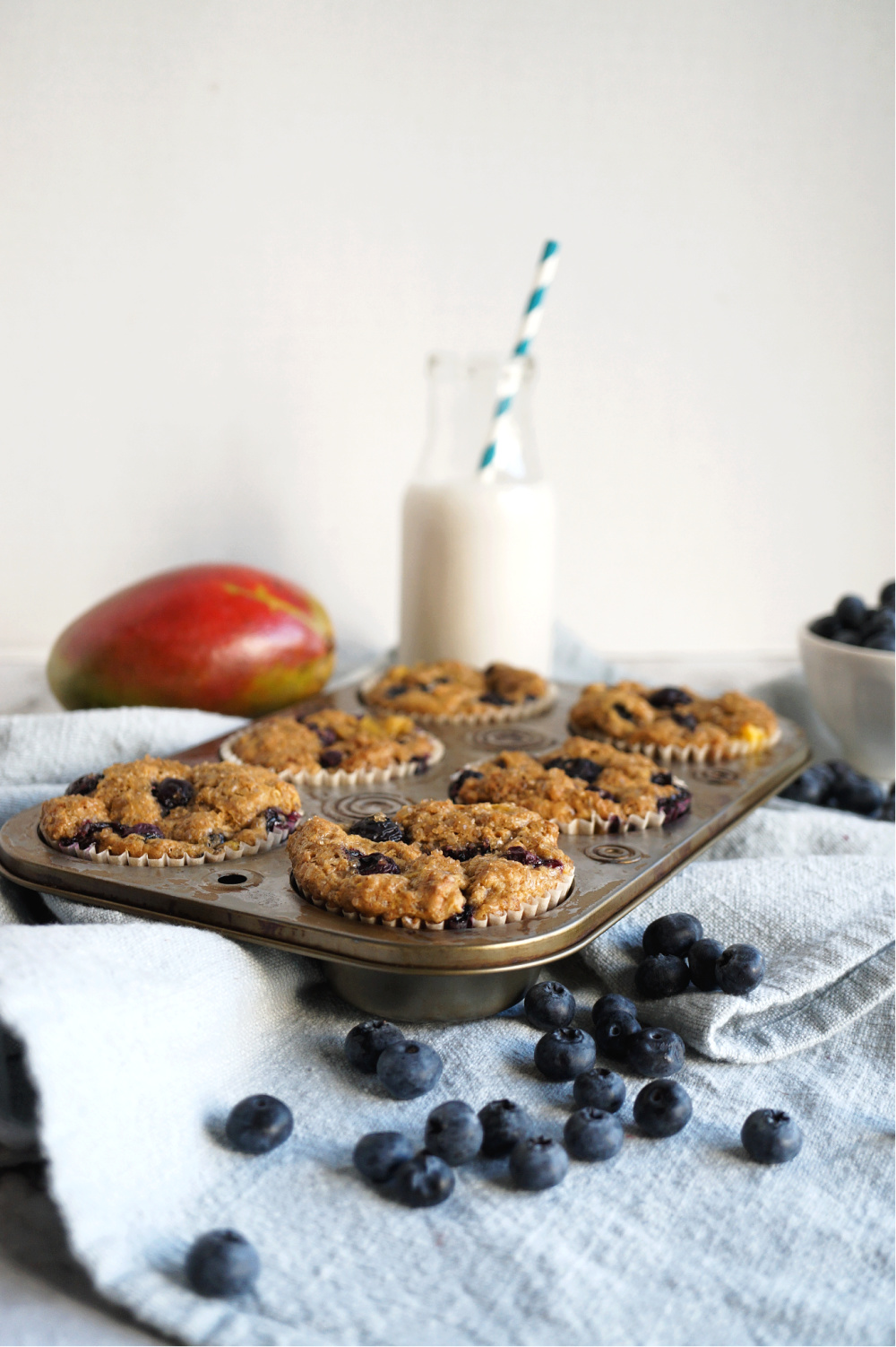 vegan blueberry mango muffins in tin with glass of milk