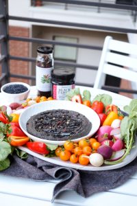 far away shot of black lentil hummus with colorful vegetables on a tray