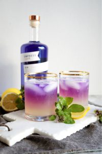 two glasses of purple basil gin fizz decorated with basil leaves and lemon slices
