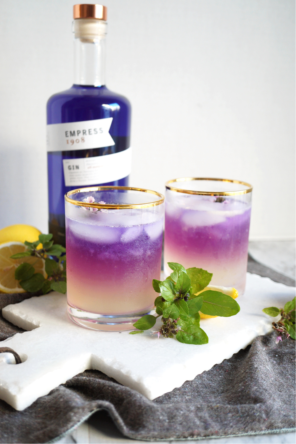 two cups of purple basil gin fizz in front of gin bottle