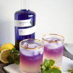 two glasses of purple and yellow gin fizz with lemons and basil leaves