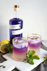 two glasses of purple and yellow gin fizz with lemons and basil leaves