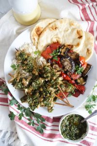 overhead shot of herb tofu skewers with chimichurri sauce, grilled vegetables, rice and naan bread