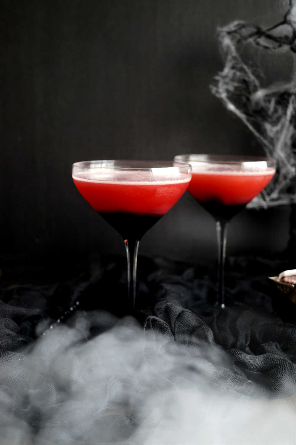 two glasses of red cocktail with spooky background and fog