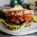 sandwich with vegan bacon, lettuce, tomato on a white plate